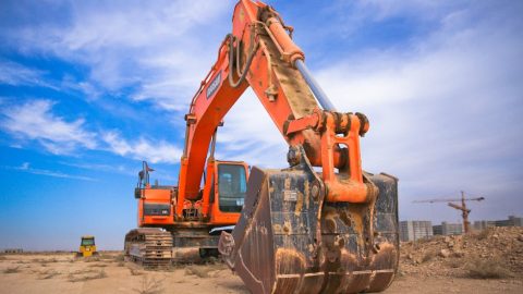 A large orange excavator working on a construction site under a blue sky.